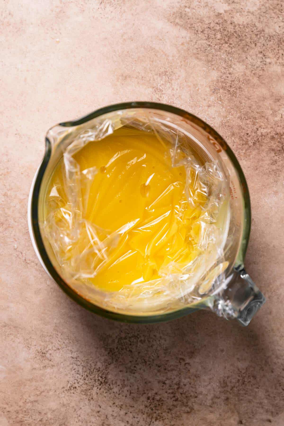 A glass bowl with the lemon curd and plastic wrap touching the top surface.