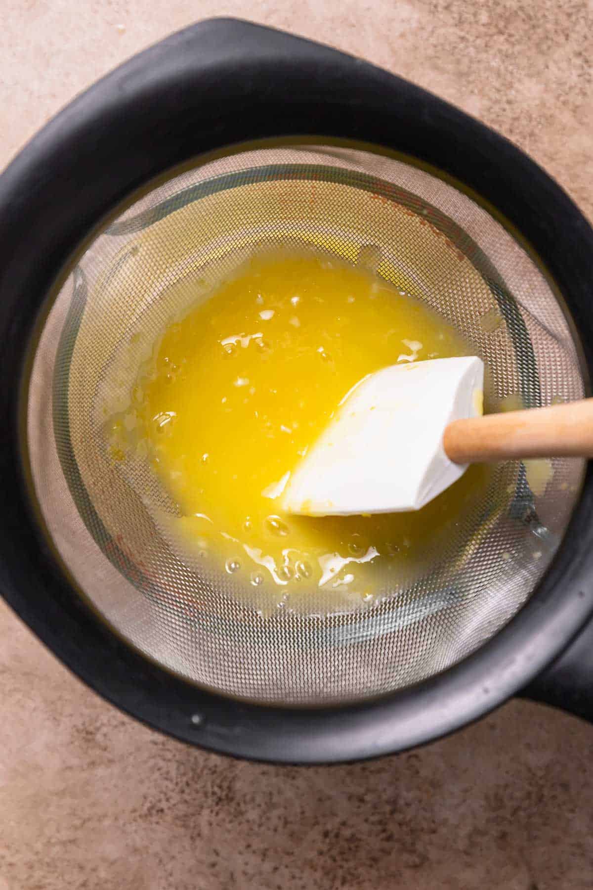 Lemon curd being pushed through a fine mesh strainer.