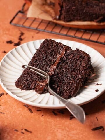 A slice of moist dark chocolate cake on a white plate with a fork digging into it.