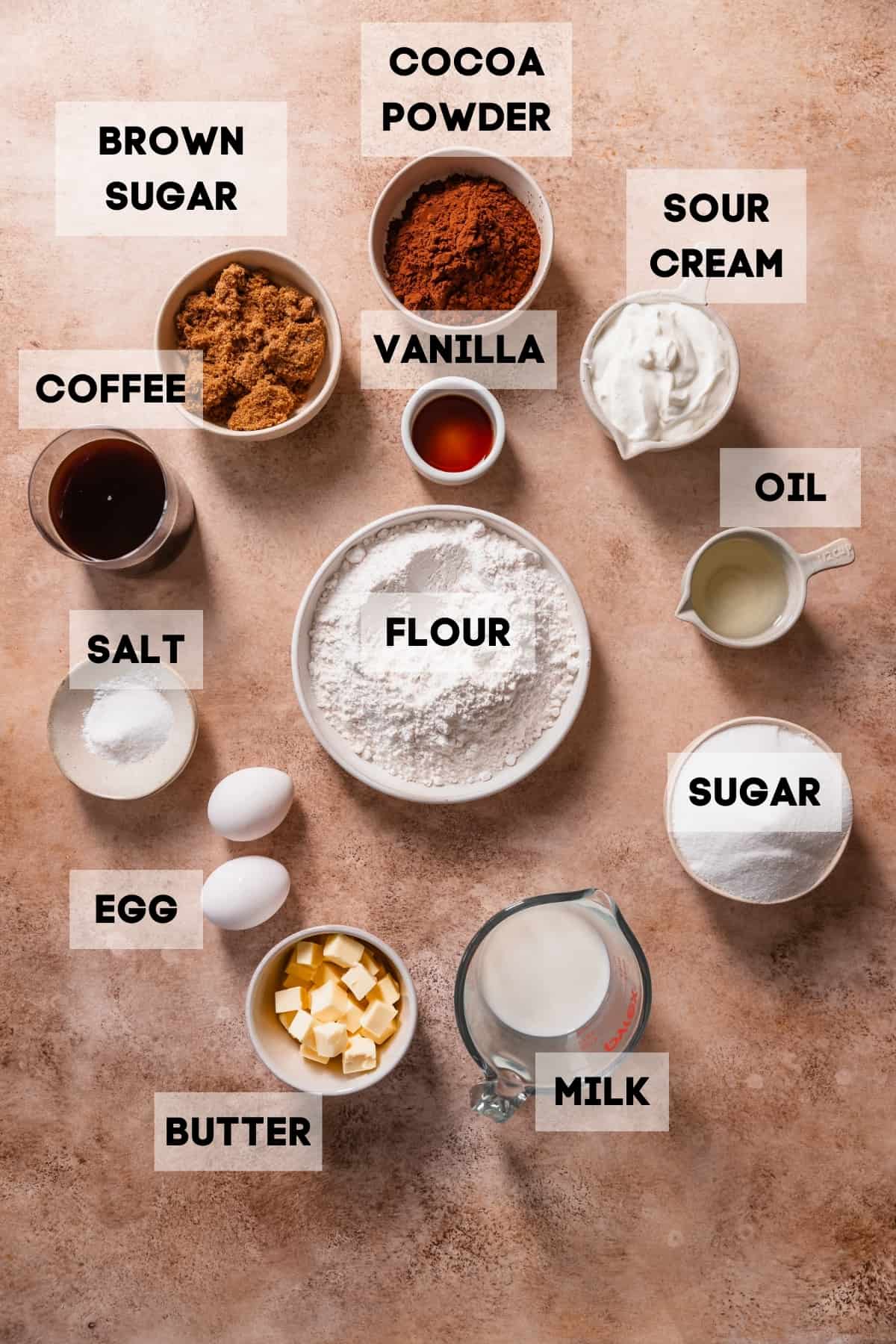 Ingredients needed to make the chocolate cake recipe in bowls with labels.