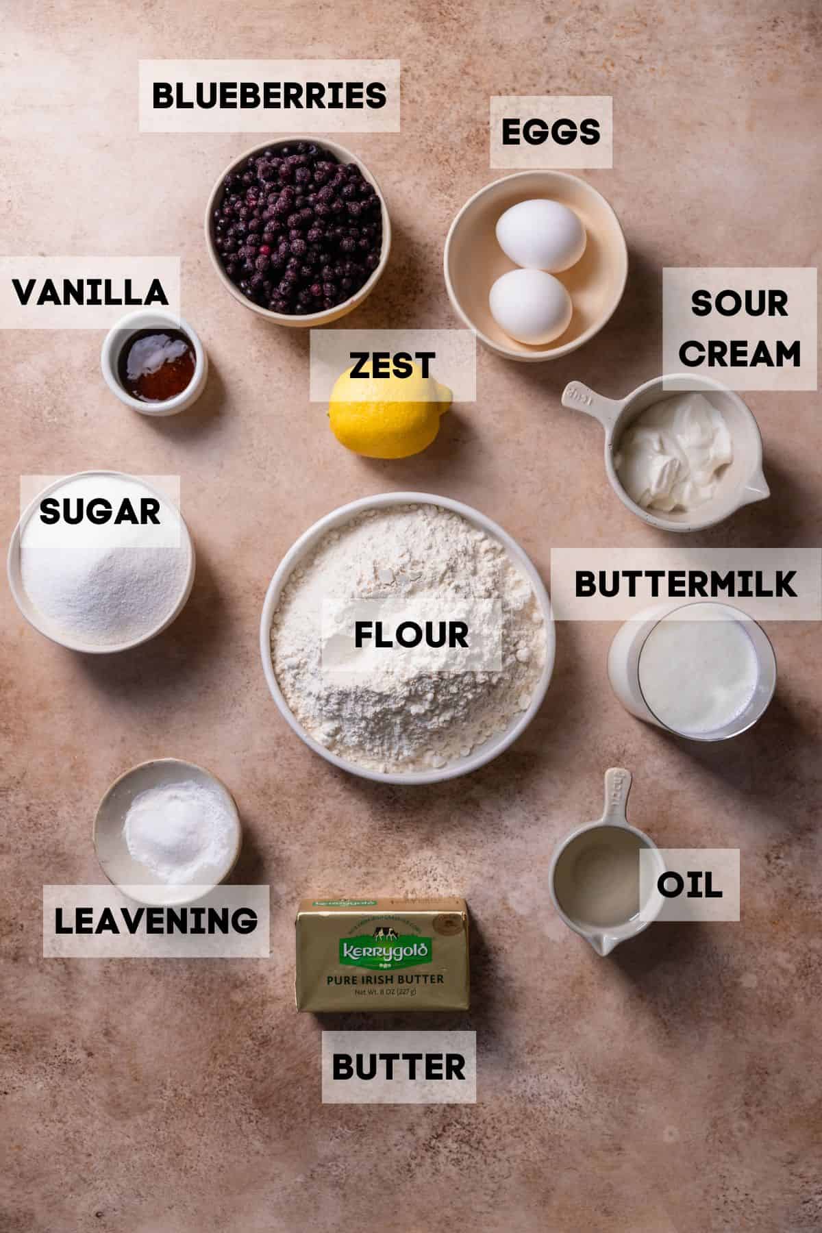 Ingredients to make moist blueberry muffins in bowls with labels.