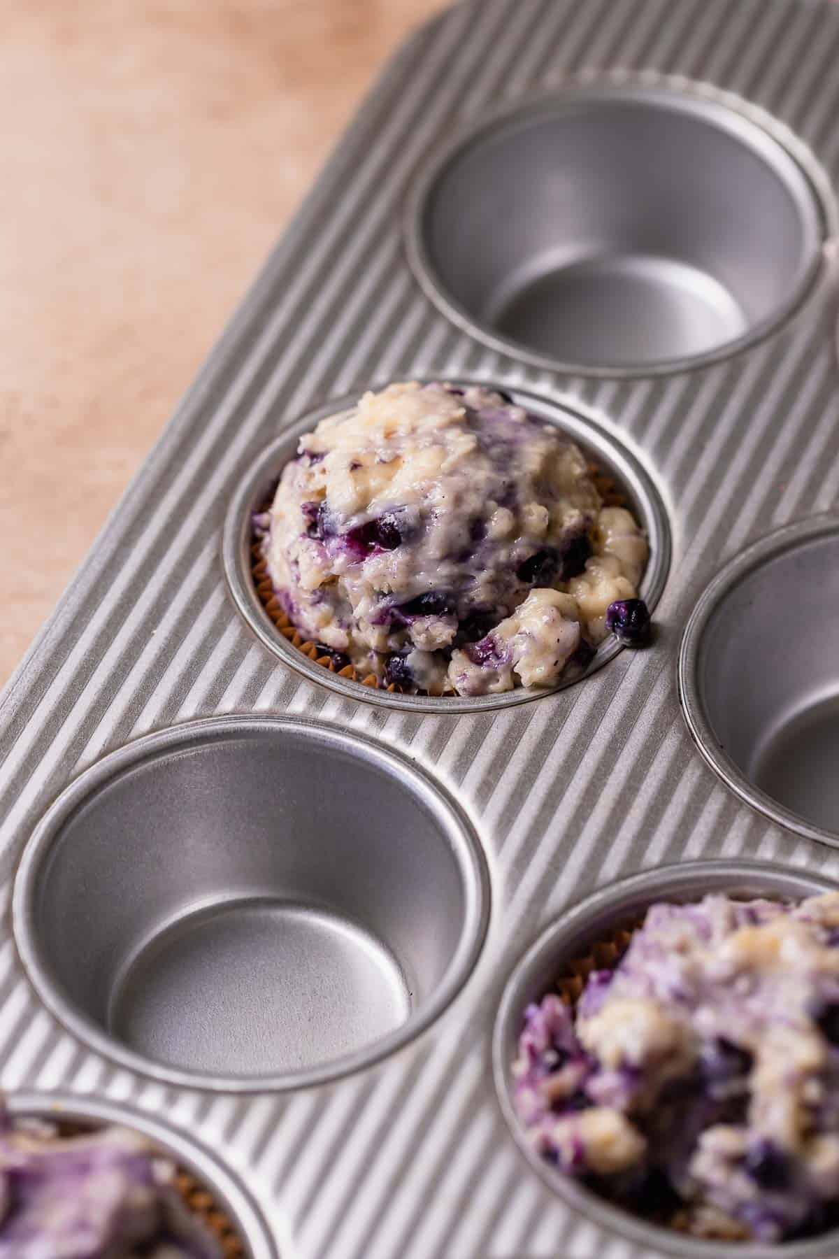 A muffin pan lined with liners and filled with blueberry muffin batter.