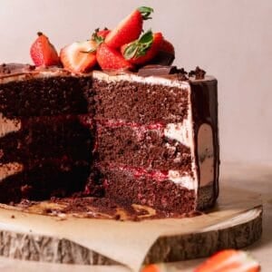 Chocolate cake with strawberry filling on a wooden cake stand.
