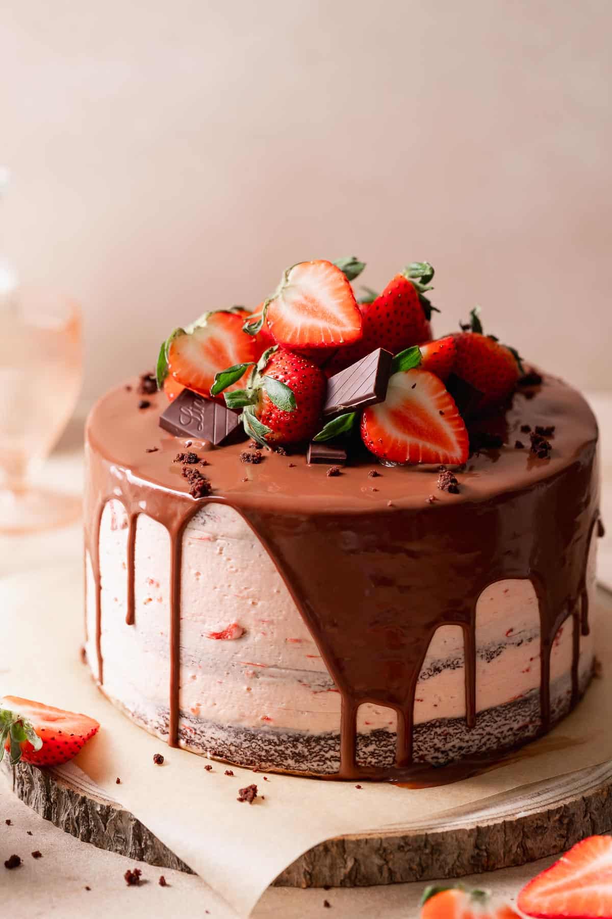 Chocolate strawberry cake with fresh strawberries and ganache on a wooden cake board.