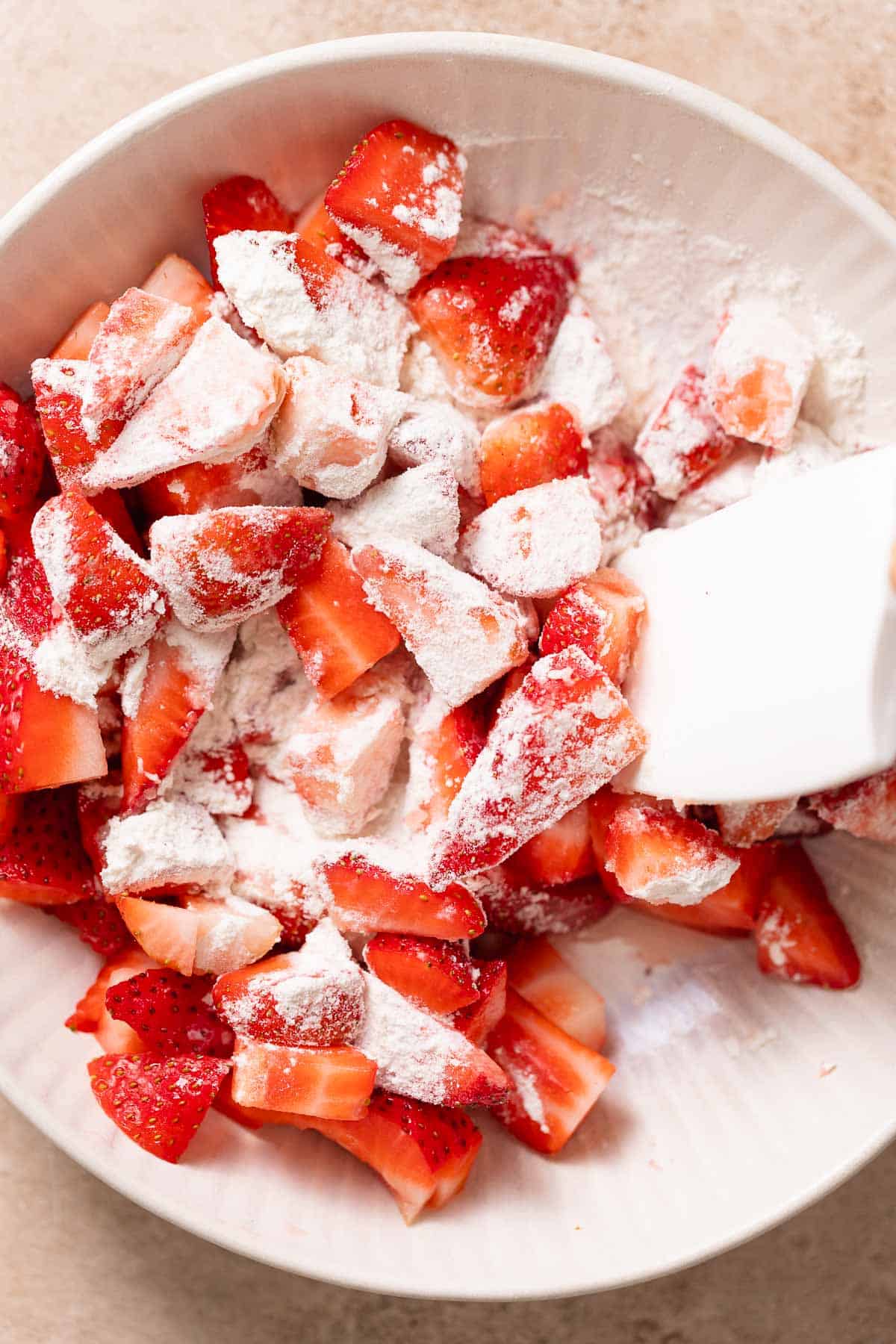 A bowl of chopped strawberries being tossed in flour and sugar.