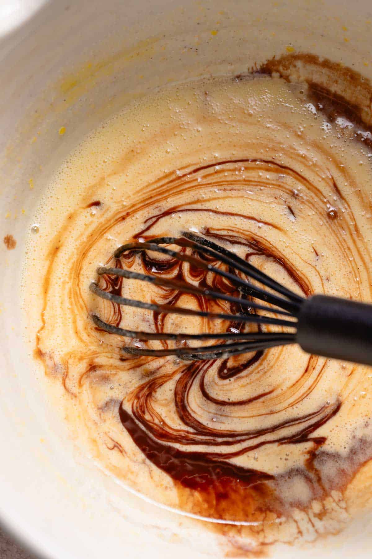 A whisk mixing the melted chocolate mixture into the eggs and sugar.