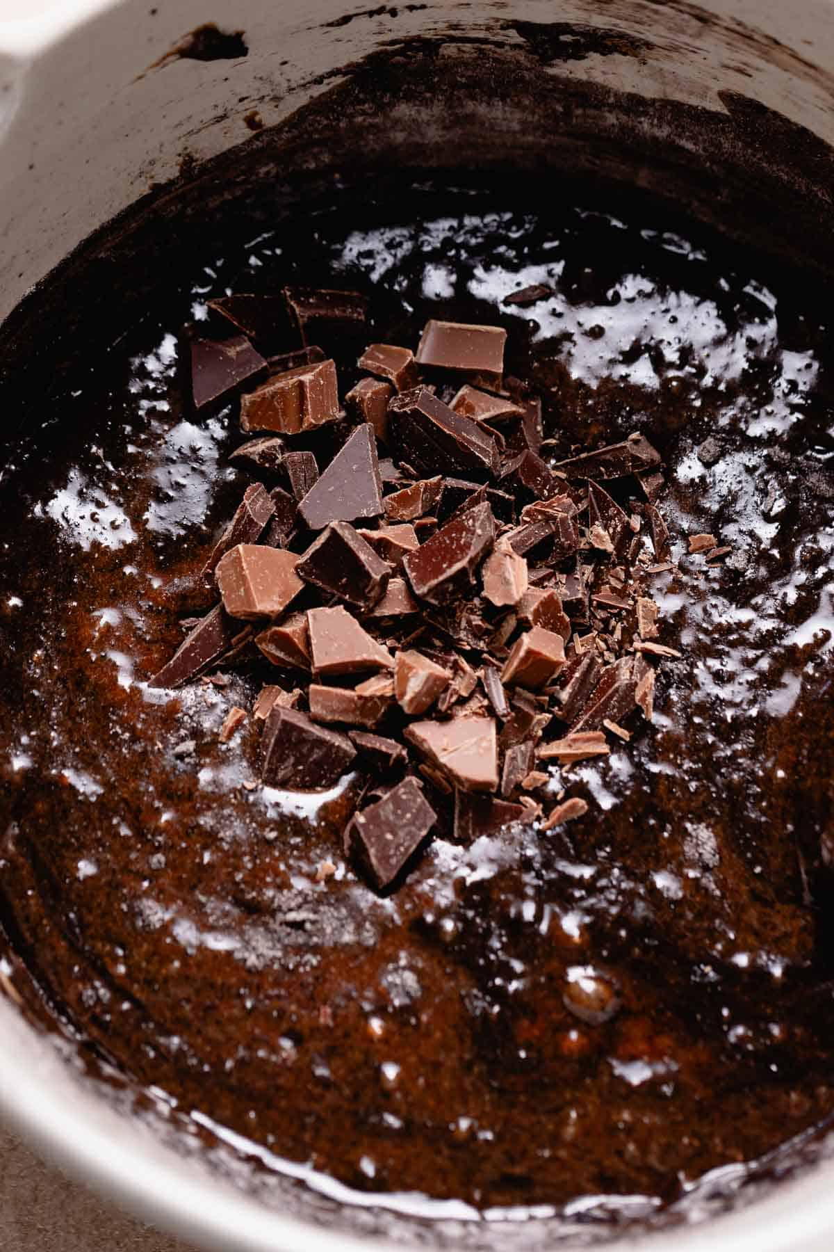 A mixing bowl of brownie batter with chocolate pieces on top before mixing.