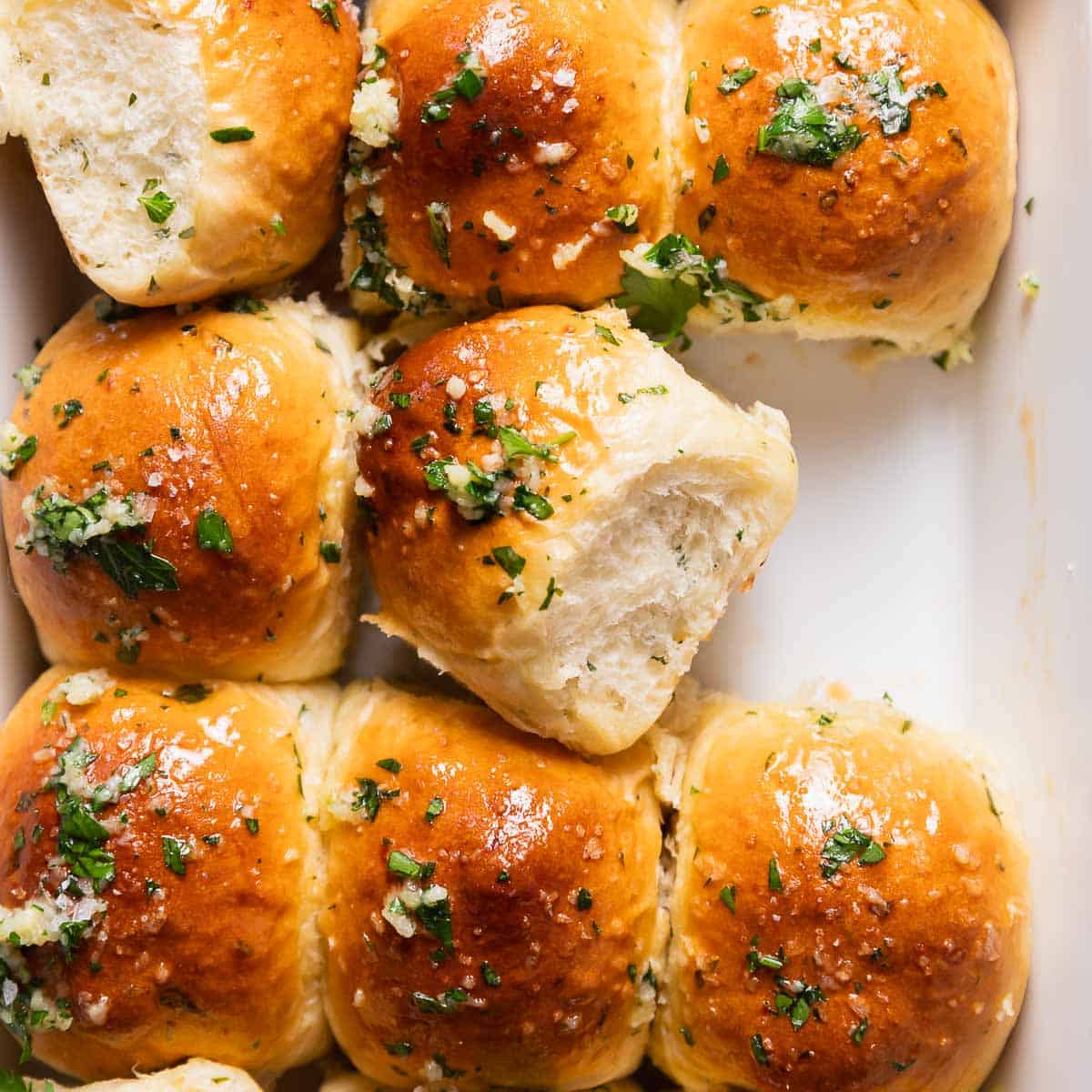 Garlic rolls brushed with garlic herb butter in a baking pan.