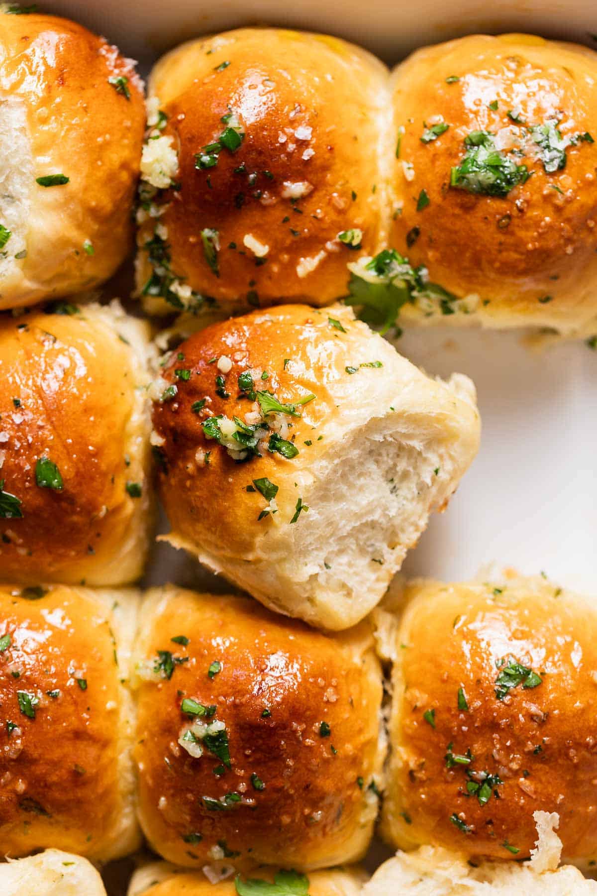 Garlic rolls covered in garlic butter and fresh parsley in a baking pan.