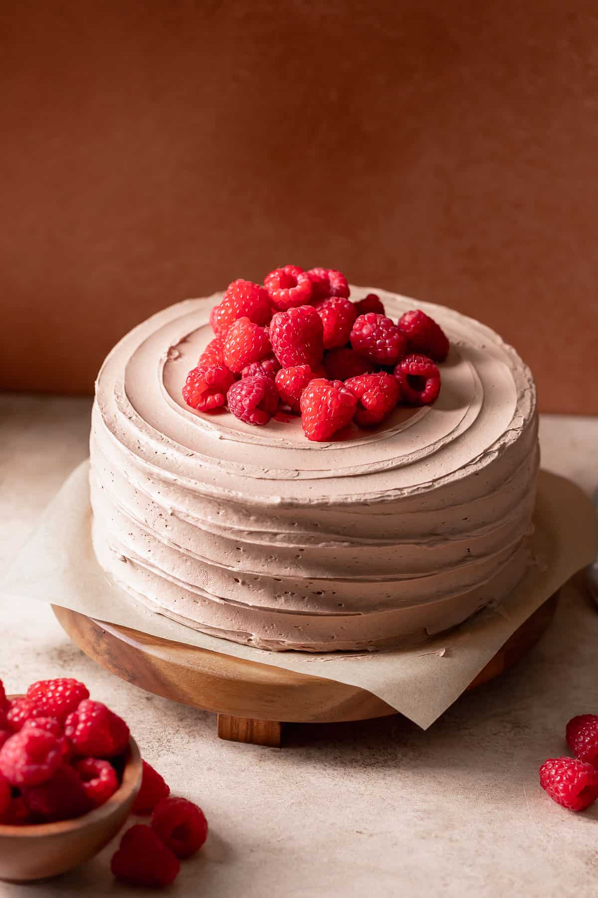Chocolate raspberry cake with fresh raspberries on top on a wooden cake stand.