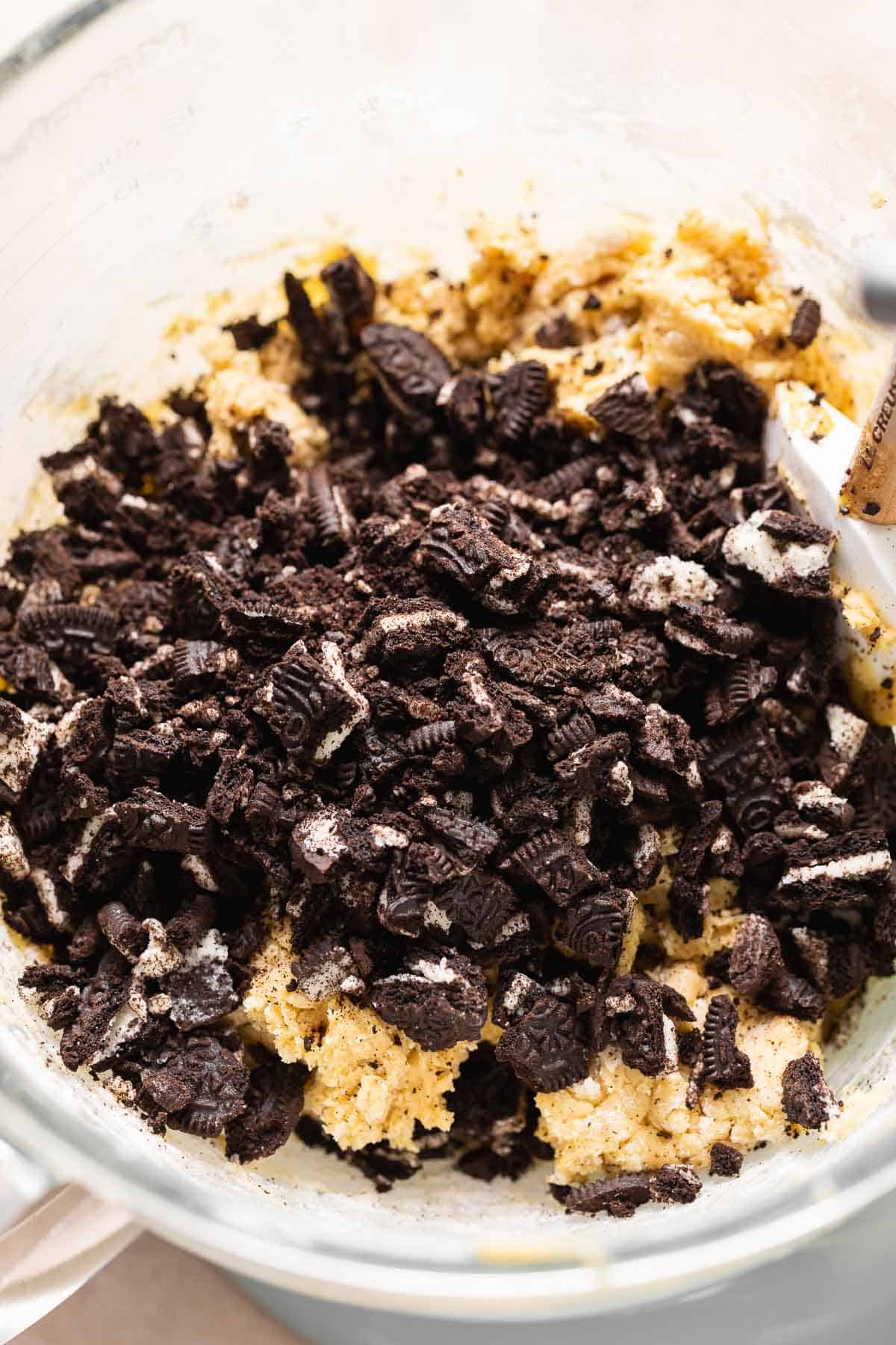 A mixing bowl with chopped oreo cookies on top of the cookie dough before mixing.