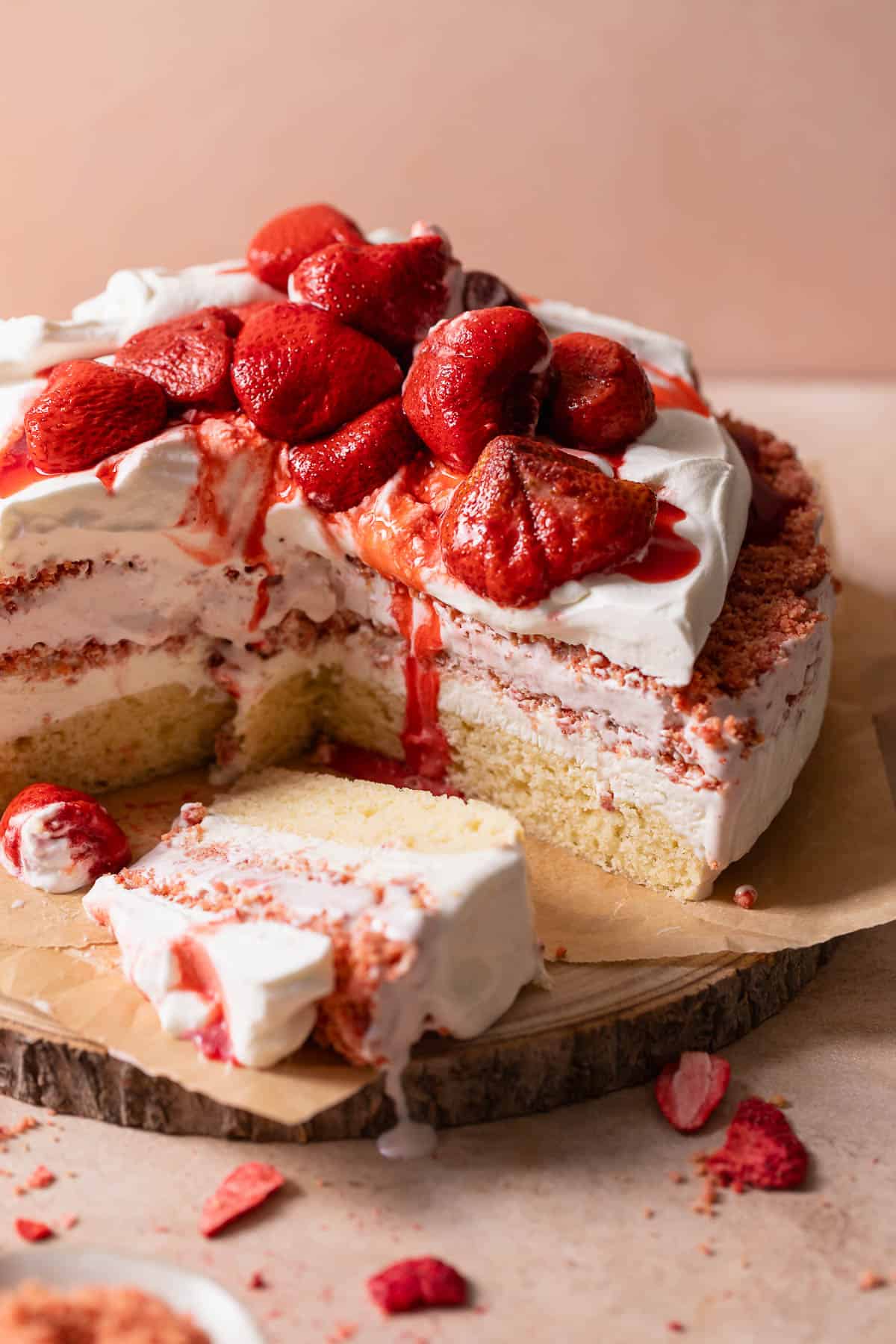Strawberry ice cream cake topped with whipped cream and strawberries on a wooden cake platter.