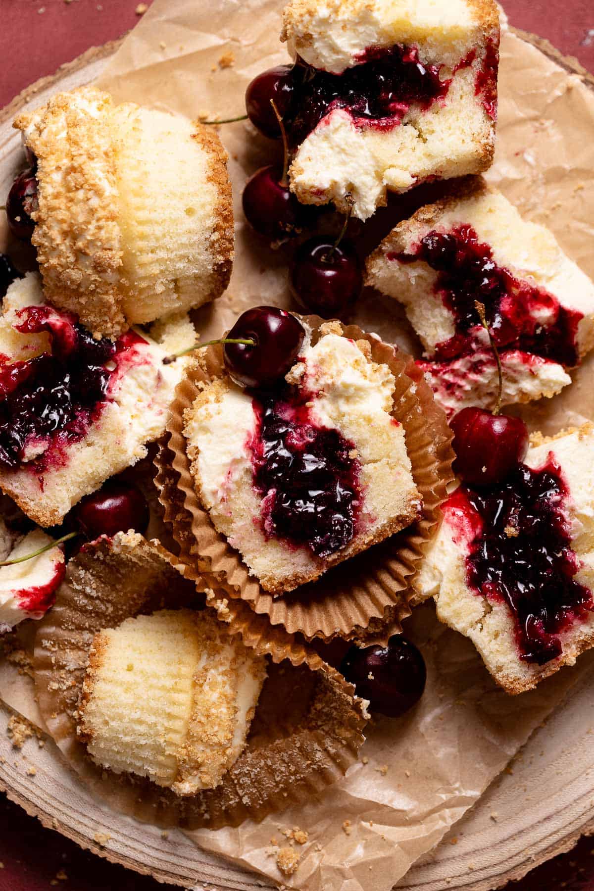 Cherry cheesecake cupcakes cut in half on a piece of parchment paper.