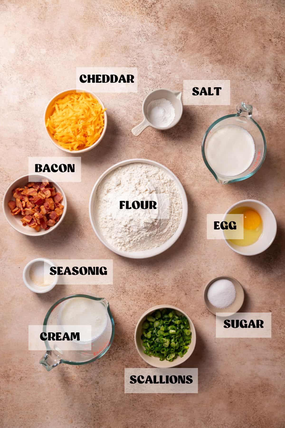 Ingredients needed to make bacon cheddar scones in bowls with labels.