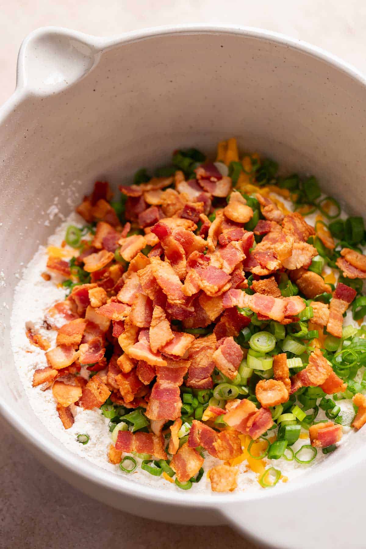 A mixing bowl with the dry ingredients, bacon, cheese, and scallions before mixing.