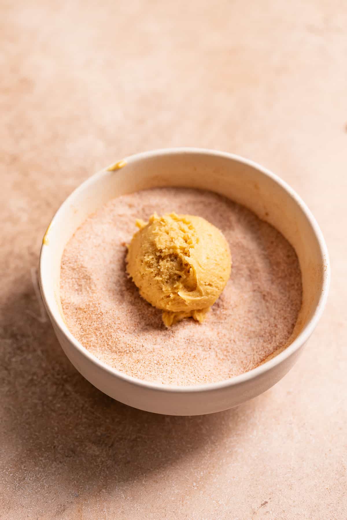 A snickerdoodle cookie dough ball in a ball of cinnamon sugar.