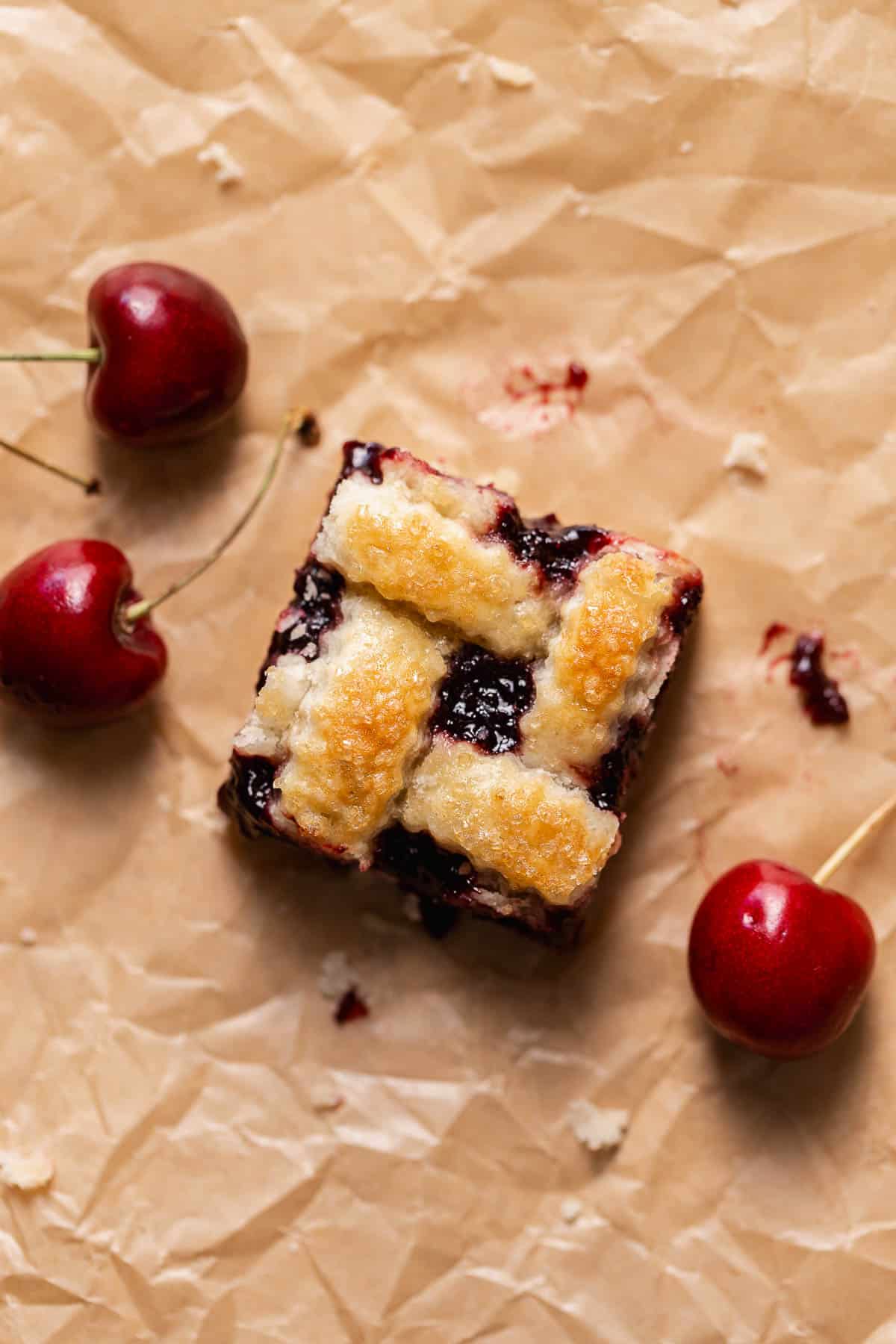 A cherry pie bar with pie crust on brown parchment paper with fresh cherries.