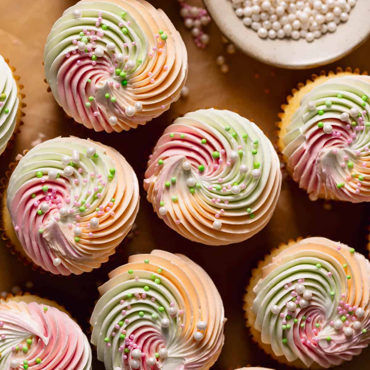 Rainbow sherbet cupcakes frosted with buttercream and decorated with pearl sprinkles.