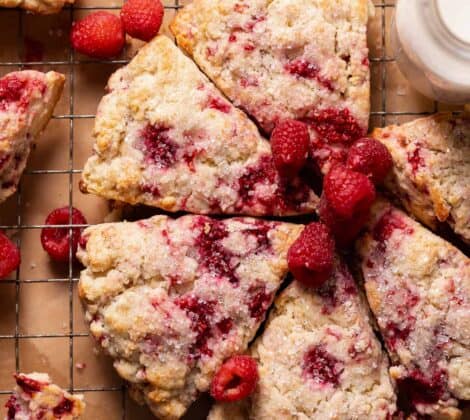 Raspberry scones topped with sugar and fresh raspberries on a wire rack.