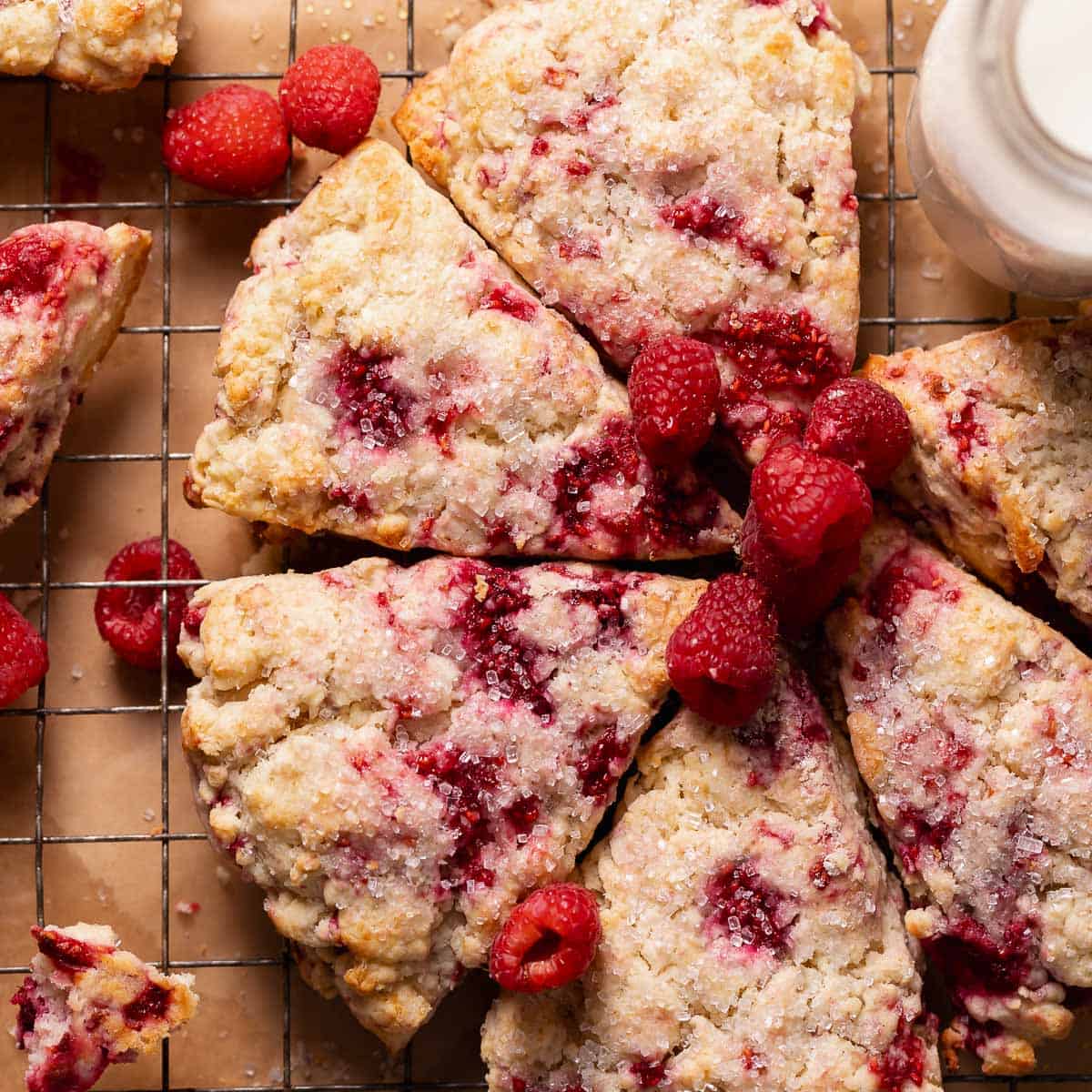 Raspberry scones topped with sugar and fresh raspberries on a wire rack.