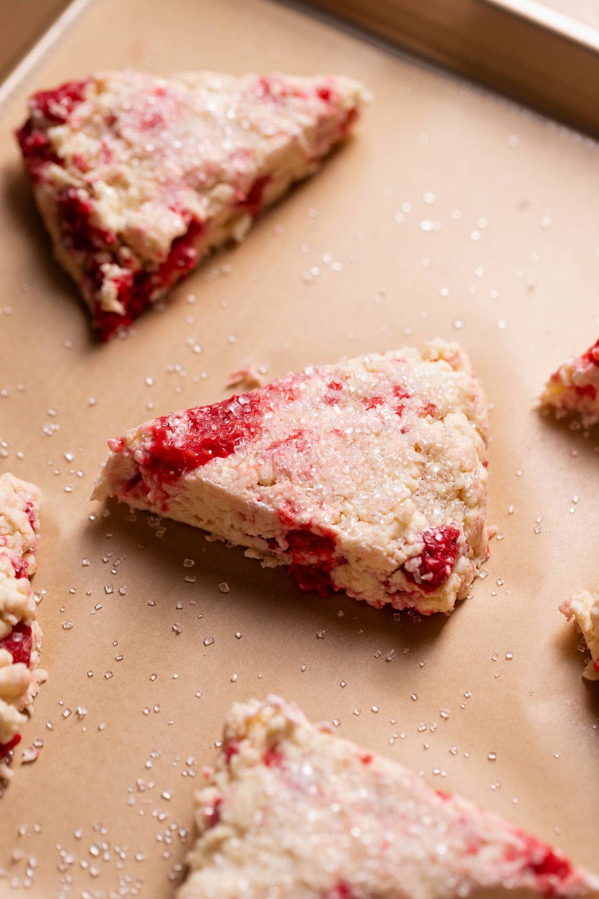 Scones with raspberries cut into triangles and sprinkled with sugar on a baking sheet.