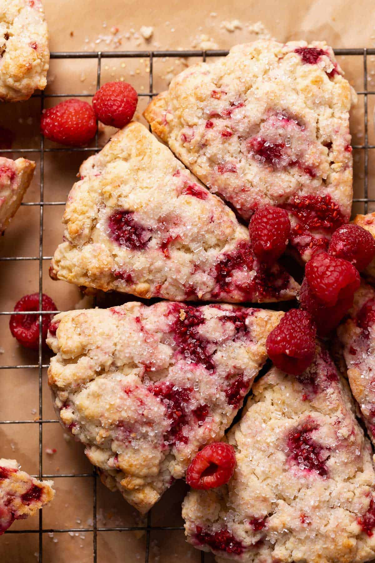 Raspberry scones topped with sugar and fresh raspberries on a wire cooling rack.