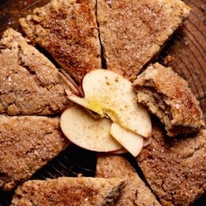 Apple cinnamon scones on a wire rack with fresh apples in the center.