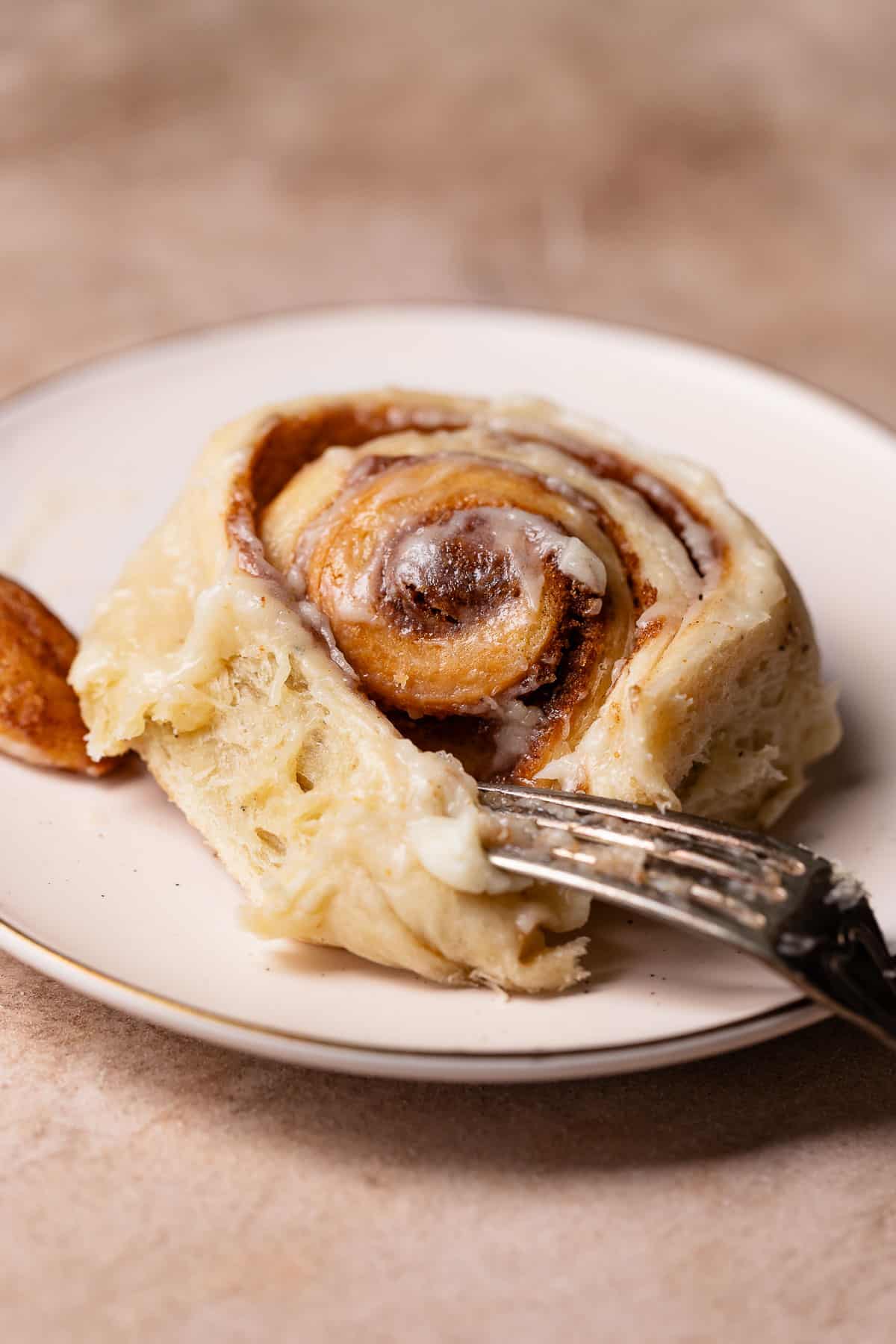 Brown butter cinnamon roll on a white plate with a fork digging into it.