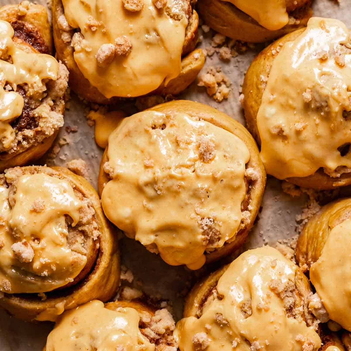 Pumpkin cinnamon rolls with cream cheese icing on a baking sheet.