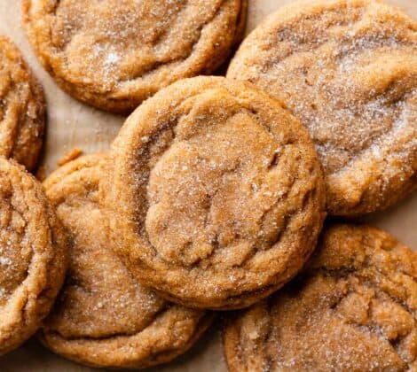 Pumpkin snickerdoodles covered in cinnamon sugar on brown parchment.