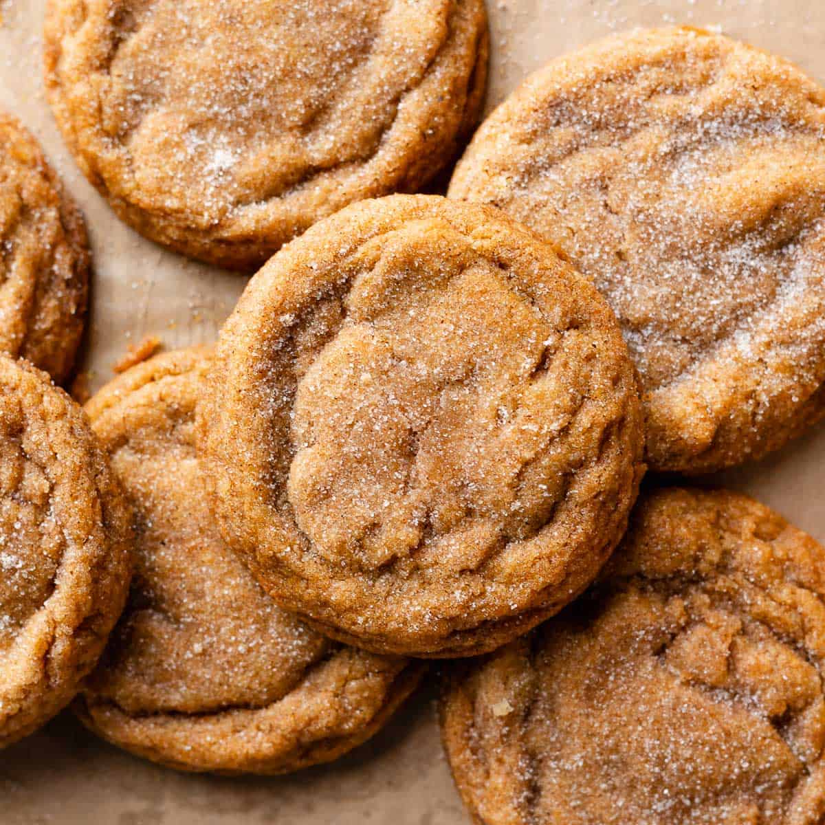 Pumpkin snickerdoodles covered in cinnamon sugar on brown parchment.