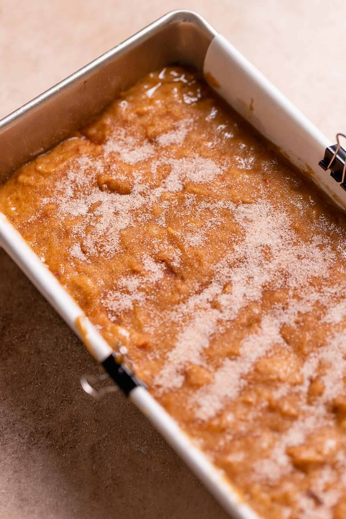 A loaf pan full of apple donut batter sprinkled with cinnamon sugar.