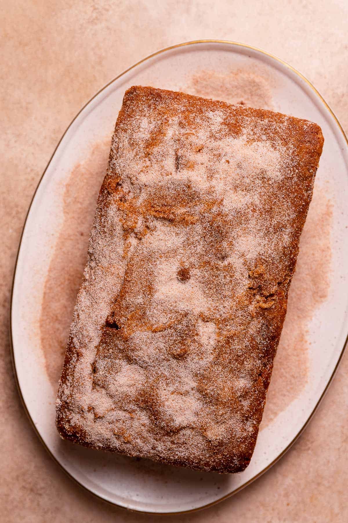 The cinnamon donut cake on a white plate being coated in cinnamon sugar.