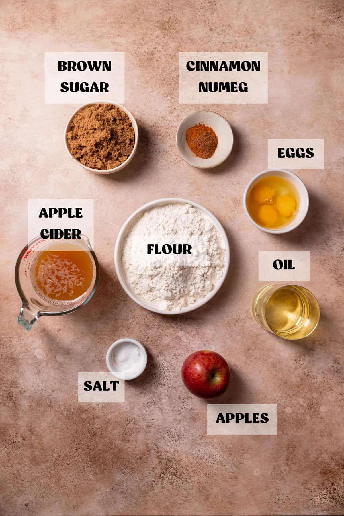 Ingredients needed to make apple donut cake in bowls with labels.