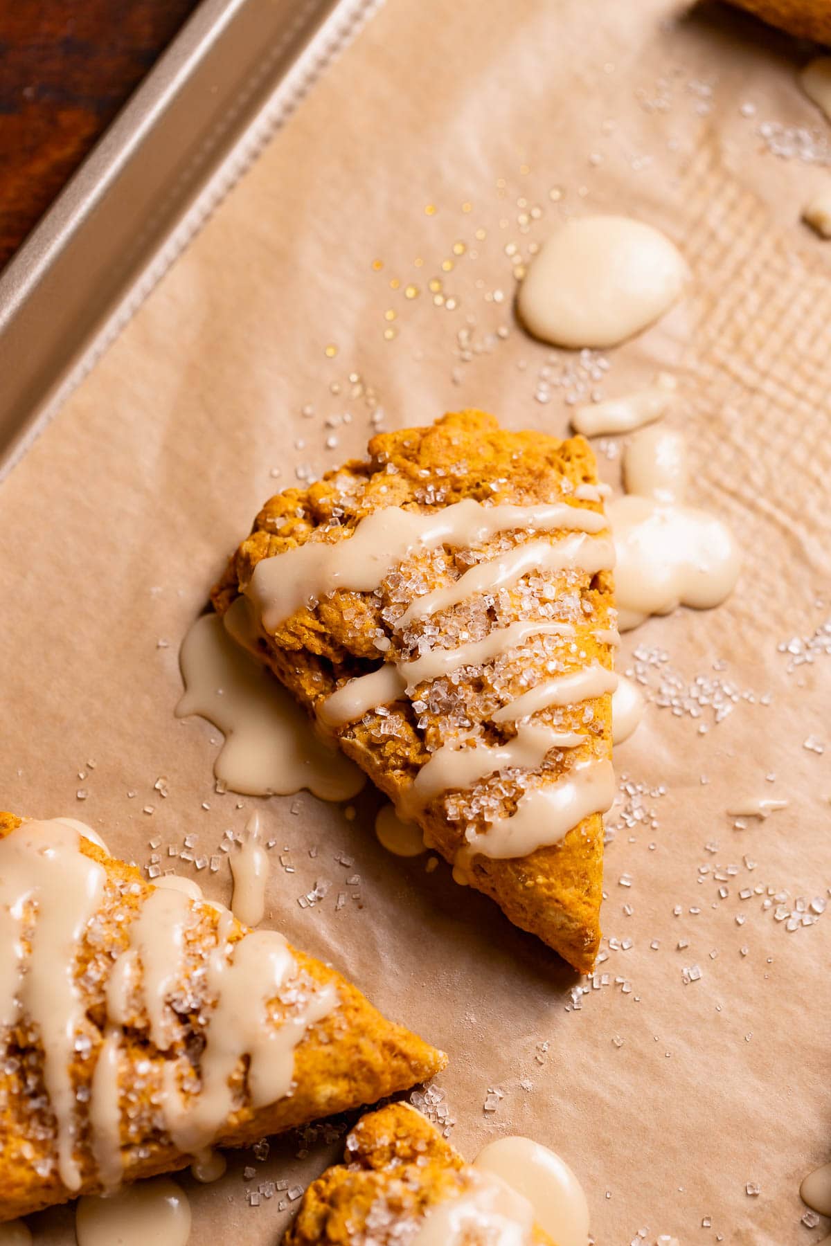 Pumpkin scones on a baking sheet drizzled with maple glaze.