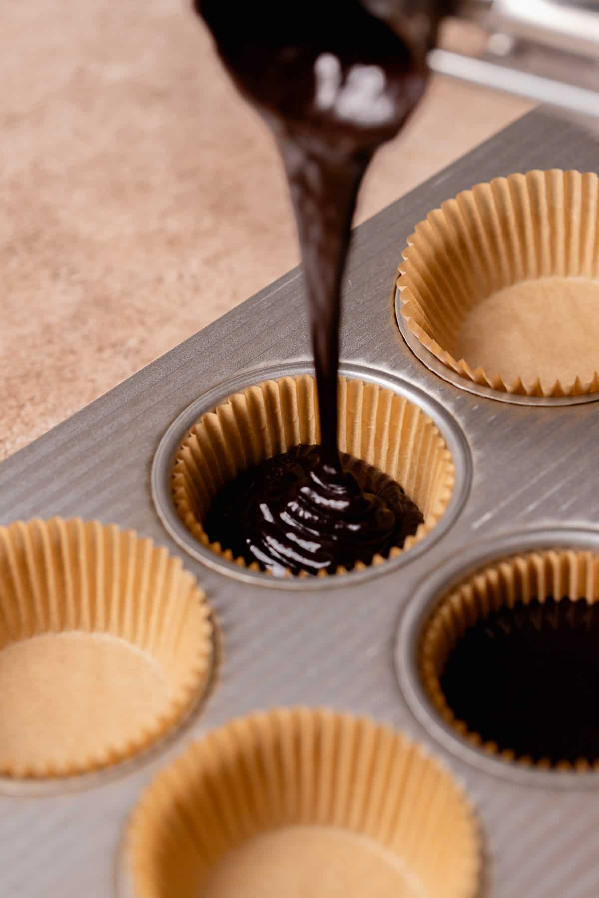 Black cupcake batter being poured into cupcake liners.