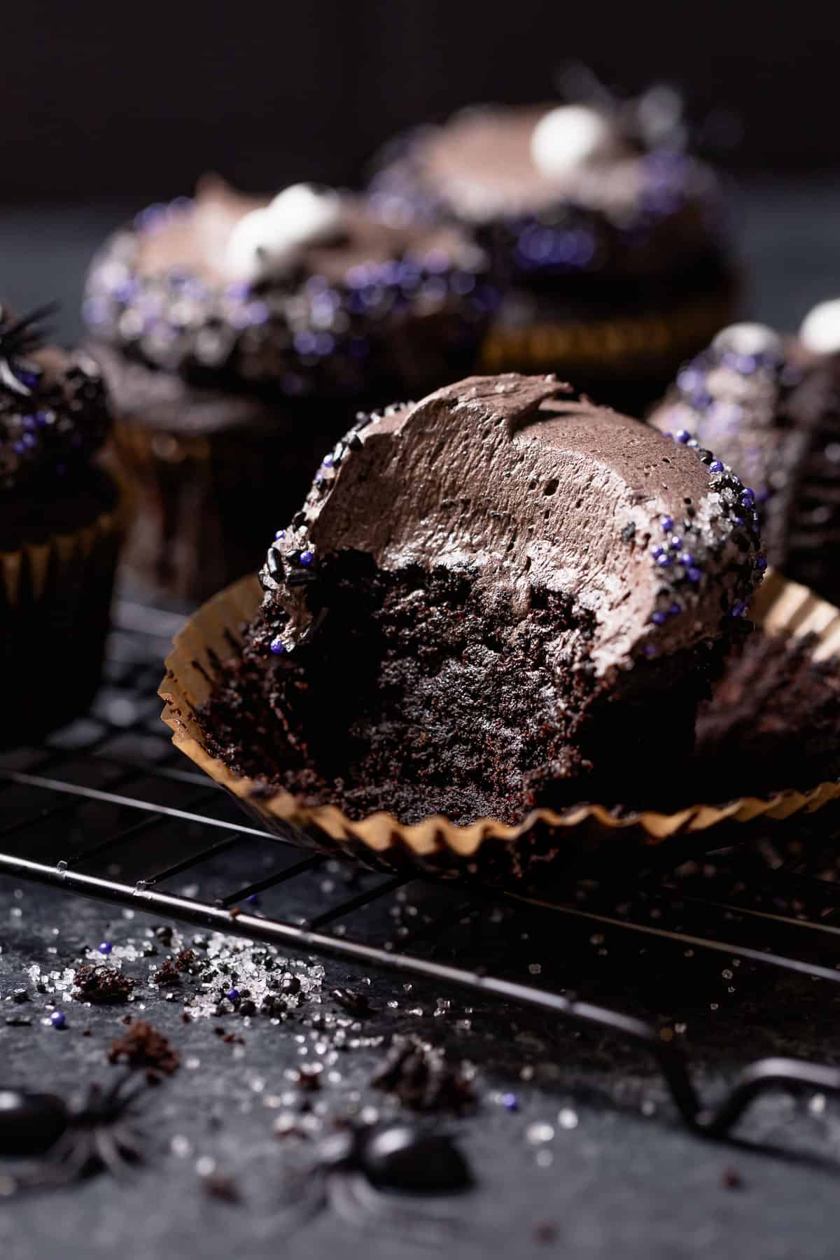 Black cupcake with a bite taken out of it on a black cooling rack.