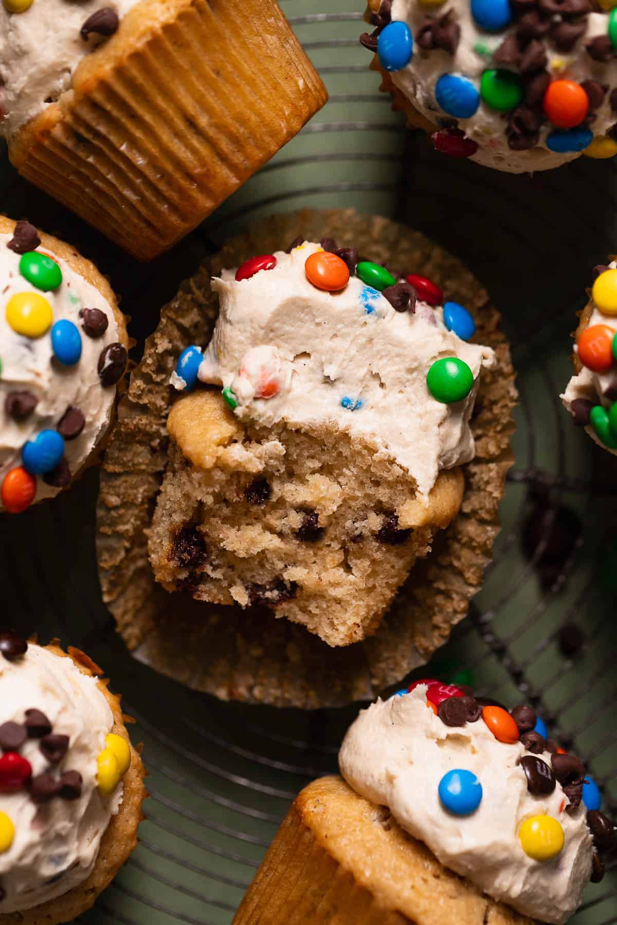 Monster cookie cupcakes on a wire cooling rack with a bite taken out of one.