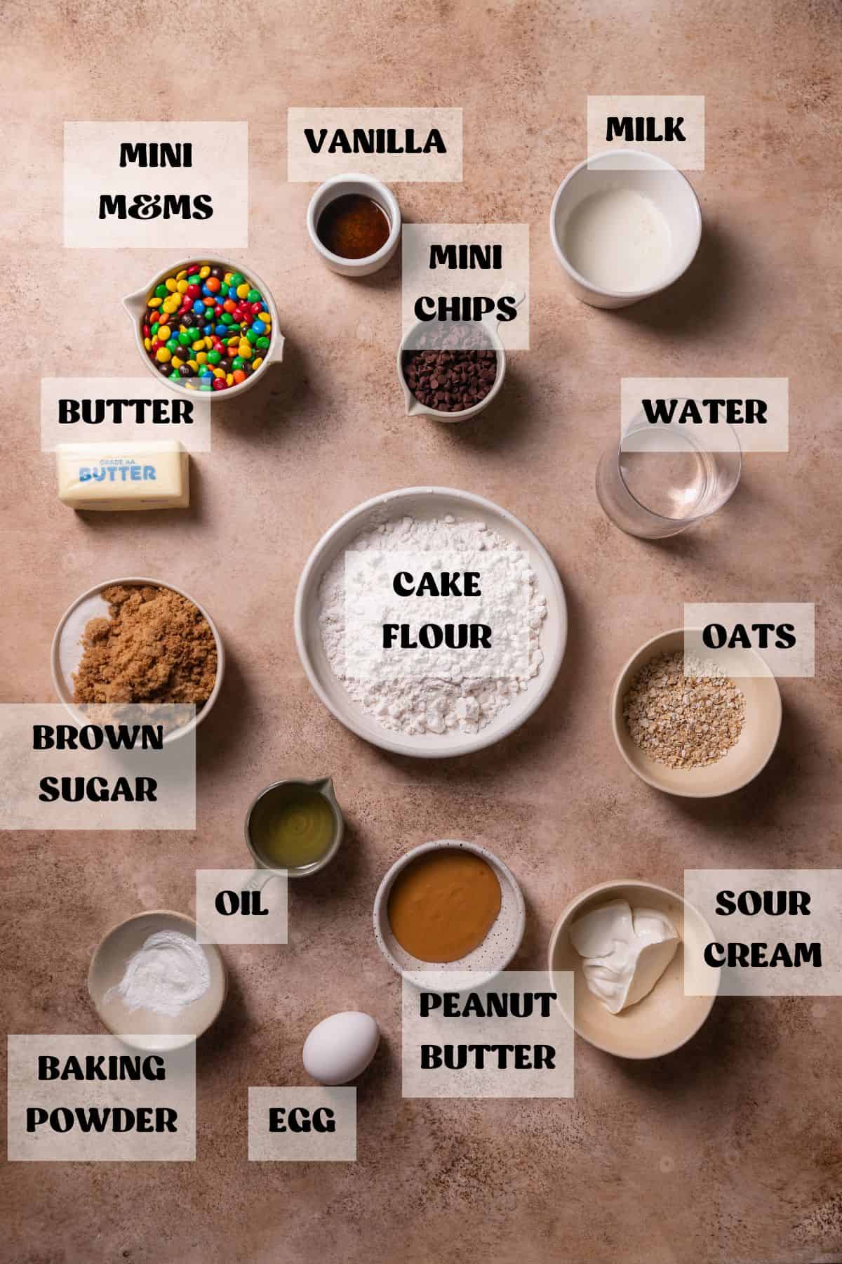 Ingredients needed to make m&m cupcakes in bowls with labels.