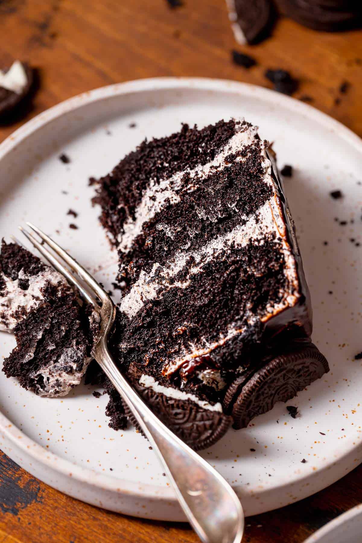 A slice of oreo cake on a white plate with a fork digging into the corner.