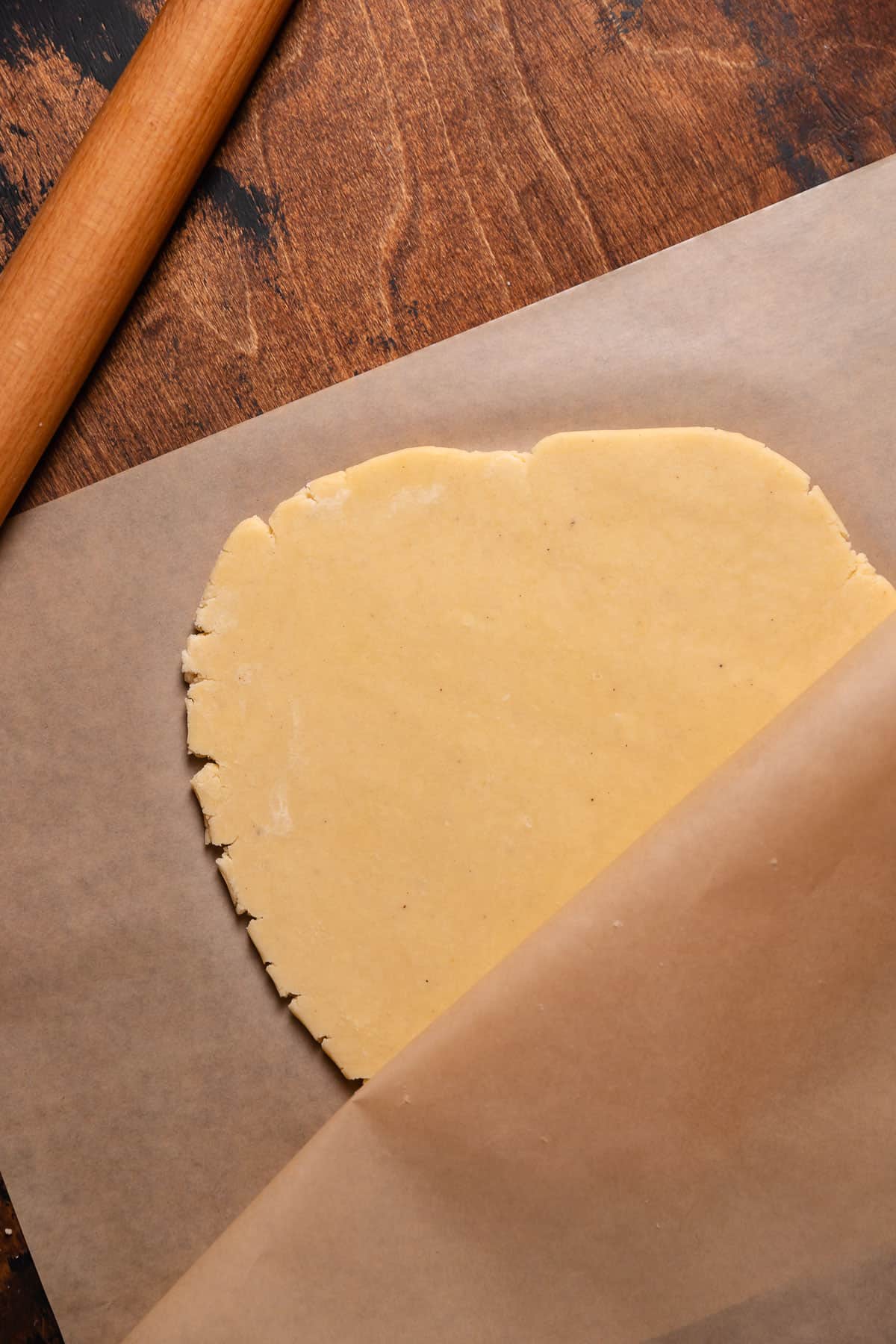 Sugar cookie dough being rolled between sheets of parchment paper.