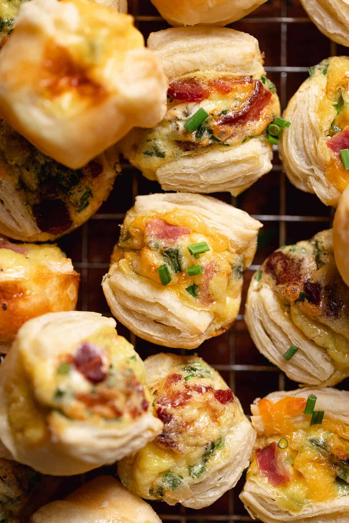 Mini quiche cups with puff pastry crust on a wire rack.