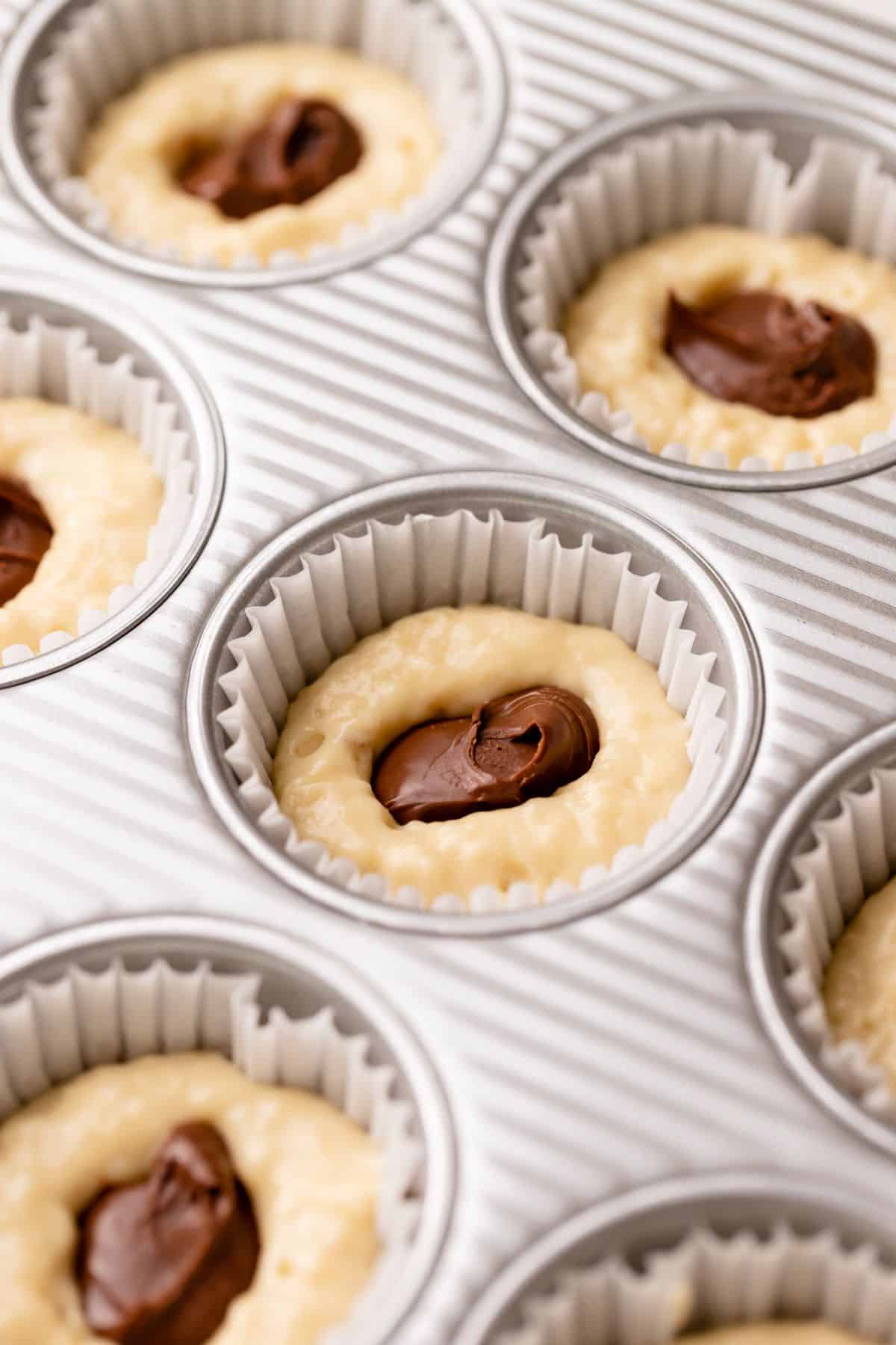 Muffins being stuffed with scoops of nutella spread.