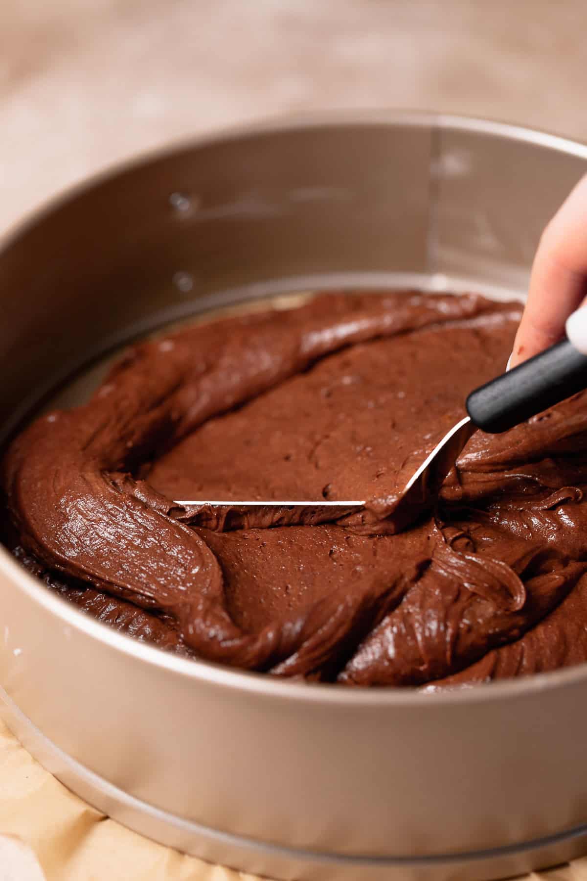 A spatula spreading the brownie batter into the baking pan.