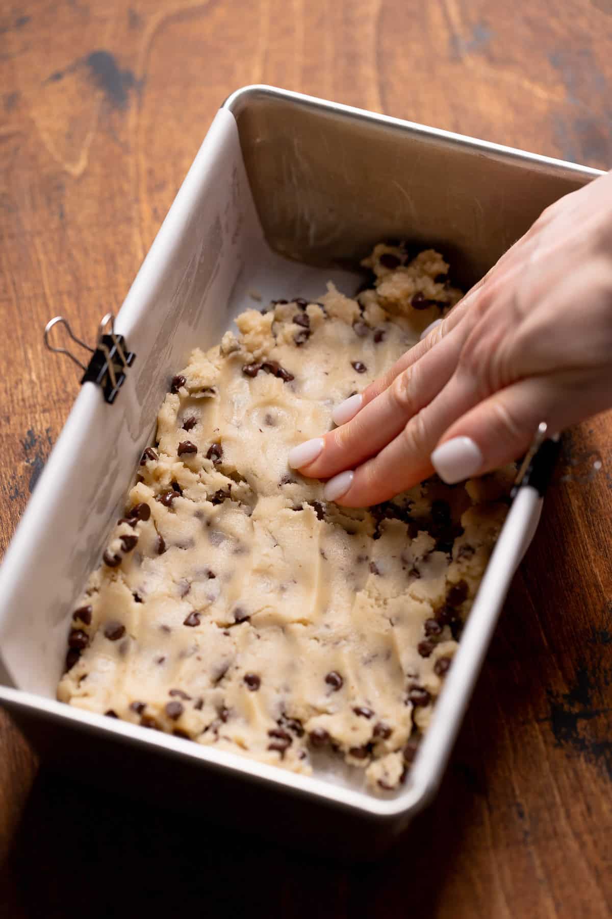 A hand pressing the cookie dough into the loaf pan.