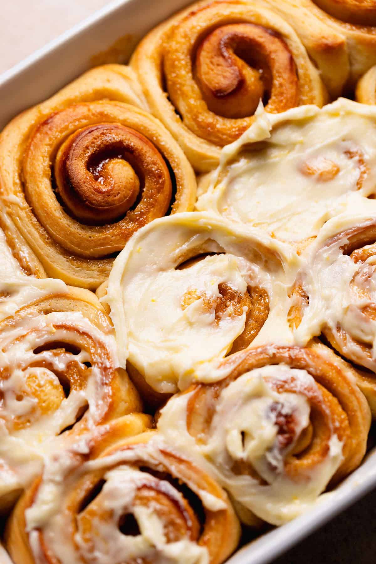 Frosting the tops of the baked rolls with cream cheese frosting.