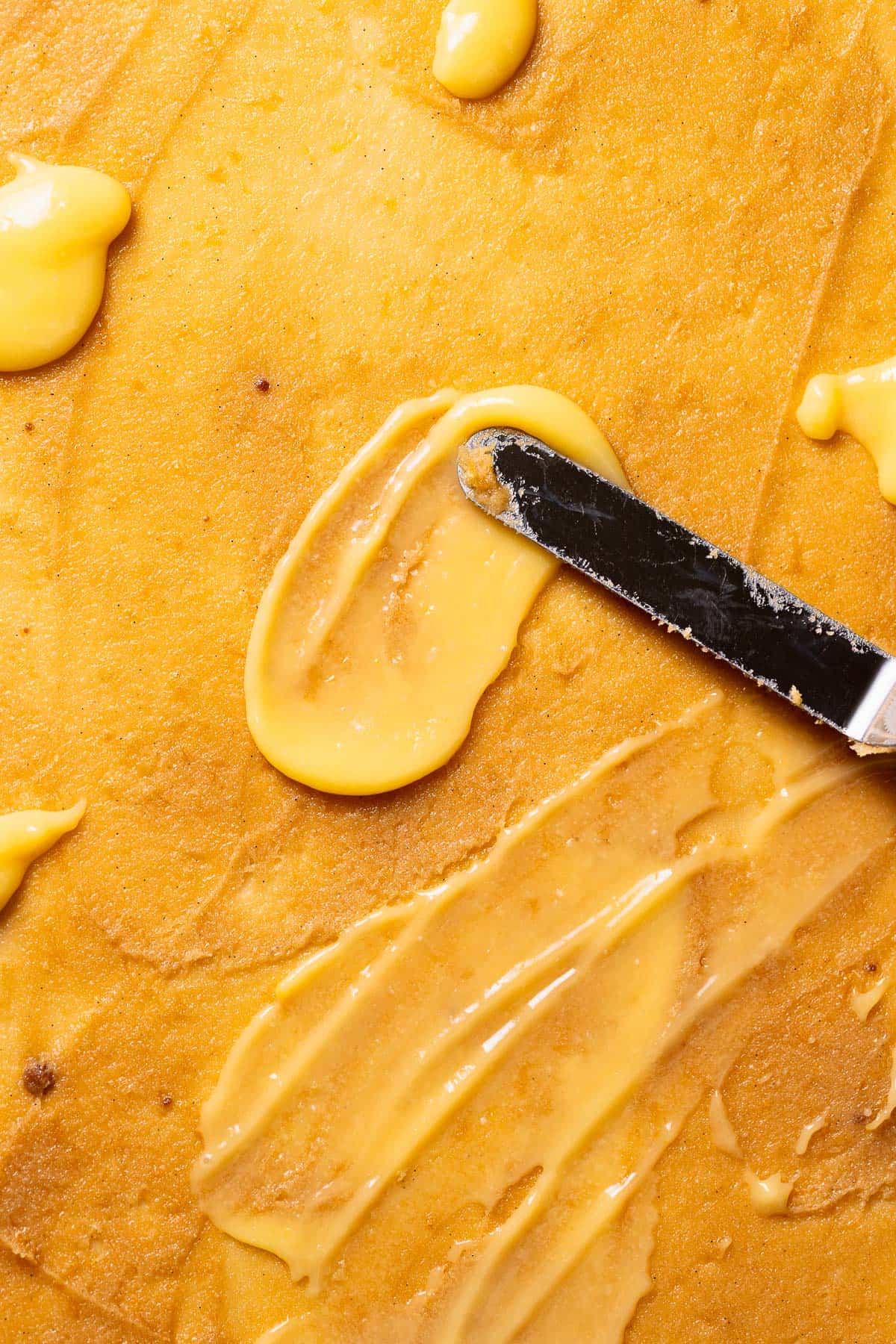 A spatula spreading the lemon filling and lemon curd across the rolled out dough.