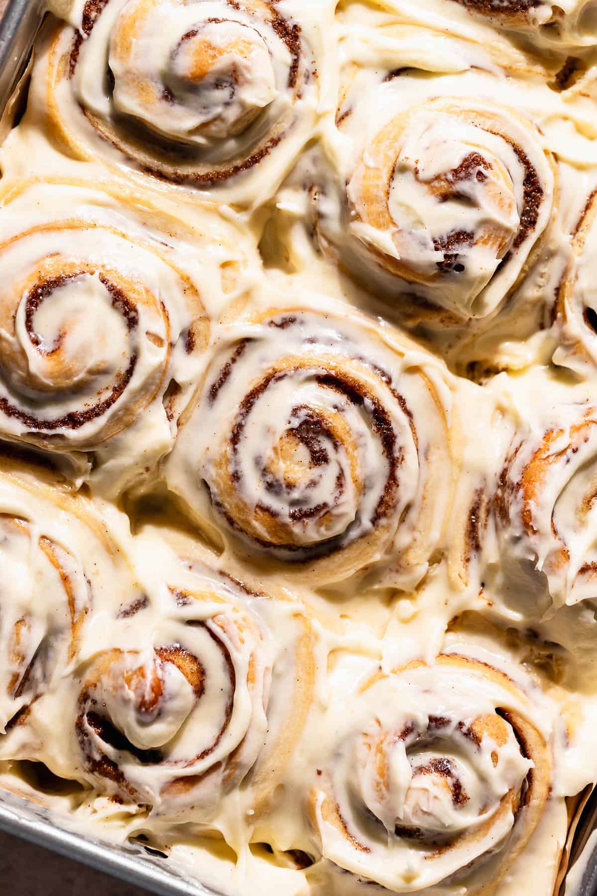 Cinnamon rolls topped with cream cheese frosting in a baking pan.