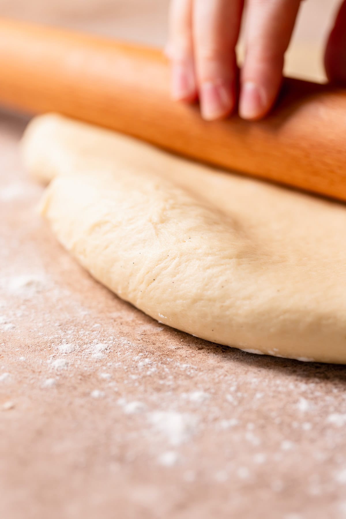 A rolling pin rolling out cinnamon roll dough.