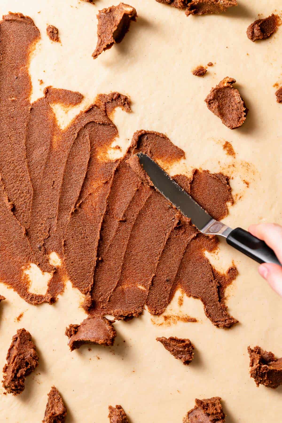 A spatula spreading the brown sugar cinnamon filling across the yeasted dough.